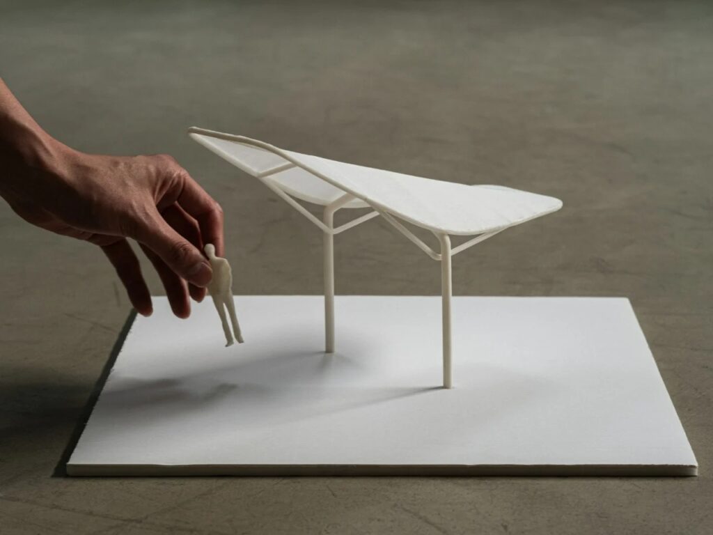 A small-scale white 3D model of the Seoul Wing canopy being held by a hand to show scale against a human figure.