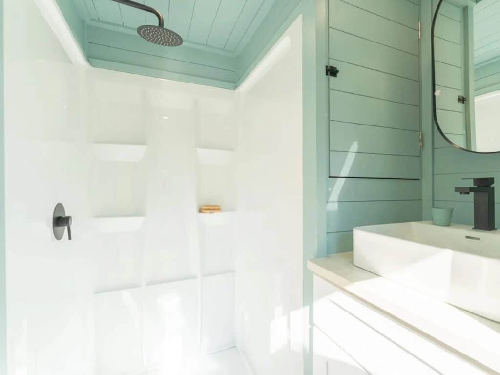 Modern tiny house bathroom with a white shower stall, turquoise shiplap walls, and a contemporary vessel sink.