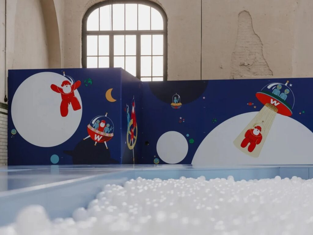 Blue walls featuring illustrations of space-themed characters and UFOs behind a white ball pit.