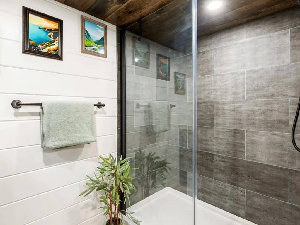 Modern tiny home bathroom featuring a gray vanity, white shiplap walls, and a glass-enclosed walk-in shower.