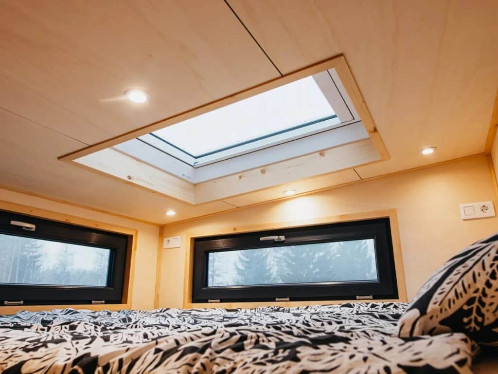 View from a loft bedroom in a tiny house, featuring horizontal windows and a large skylight for stargazing and natural light.
