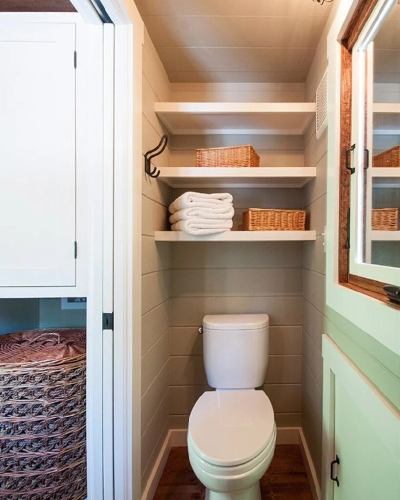 Small bathroom interior showing a white toilet and open shelving for storage in the Ynez tiny house.