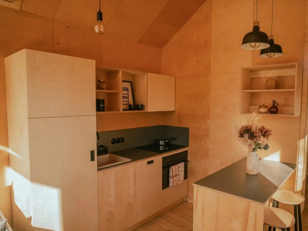 Minimalist kitchen in a tiny house with light wood cabinets, black countertops, and integrated appliances.