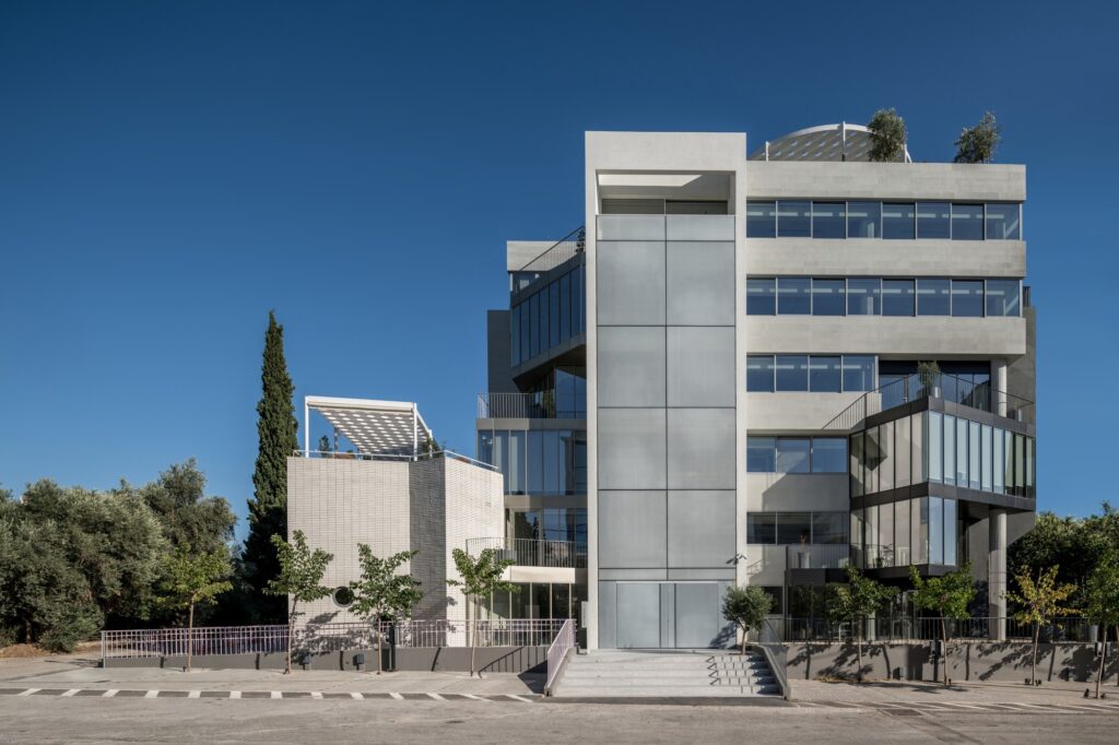 The main entrance of the Art1 office building with a massive frosted glass wall, wide steps, and minimalist landscaping under a clear blue sky.