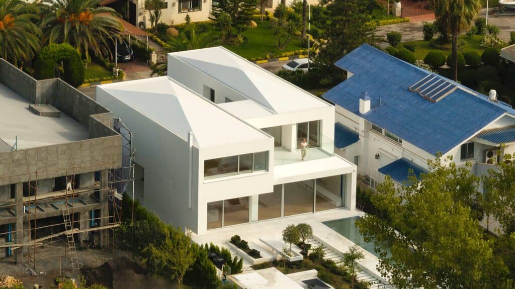 Side aerial view of the villa showing the multi-level white volumes and the relationship with adjacent buildings.