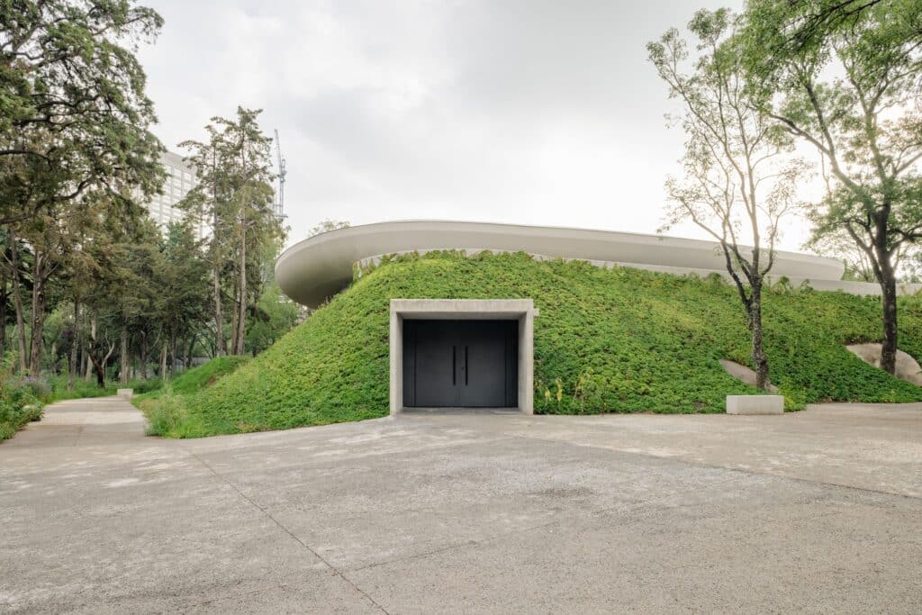 A concrete entrance portal set into a hill completely covered in green groundcover plants under a curved roof.