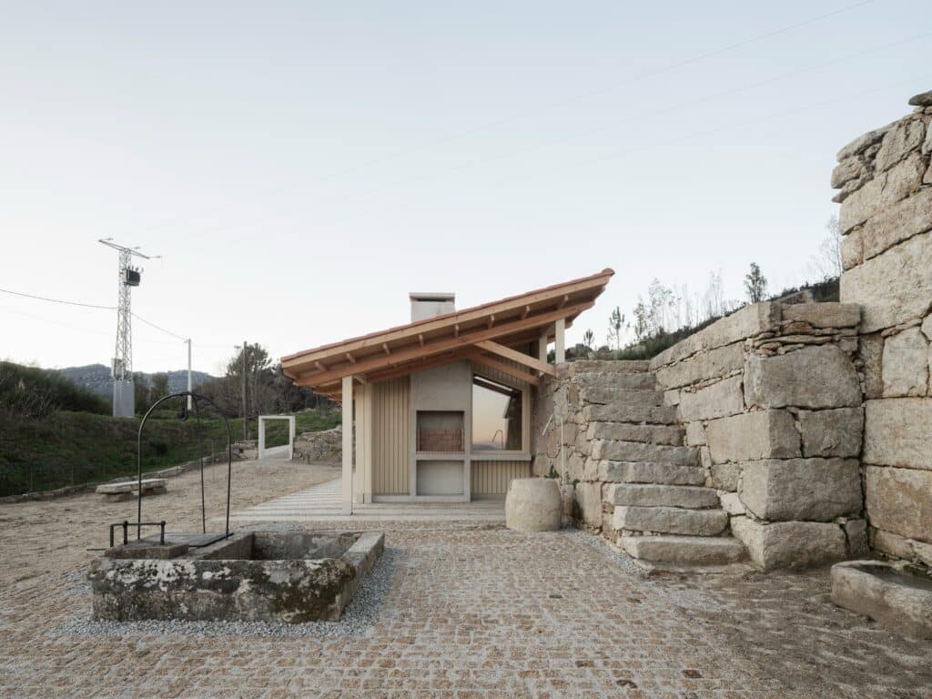 Side view of the pavilion showing the sloped tiled roof, an outdoor stone fireplace, and a traditional washing well.