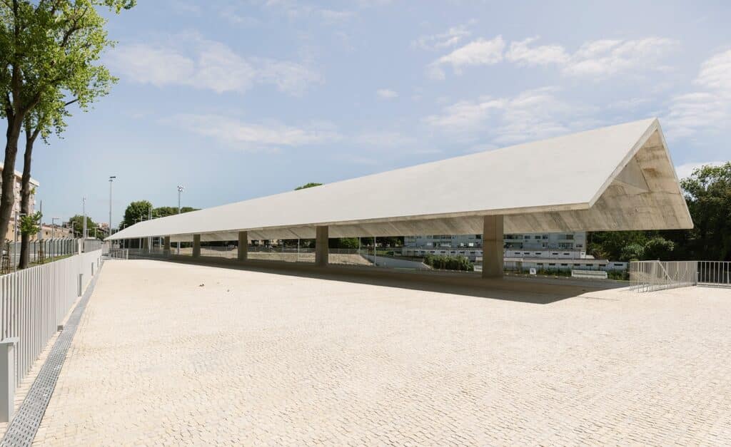 Wide shot of the expansive concrete plaza and the long pavilion structure at Ramalde Sports Park.