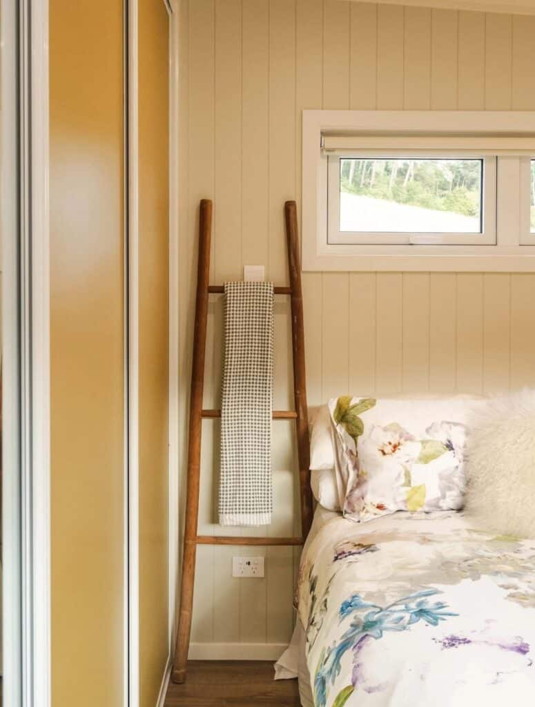 Detail of a cozy bedroom area with a wooden ladder towel rack and natural light from a high-placed window.