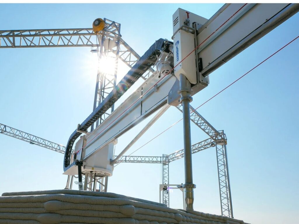 Low angle shot of the 3D printing crane against a bright sun, highlighting the futuristic nature of the construction process.