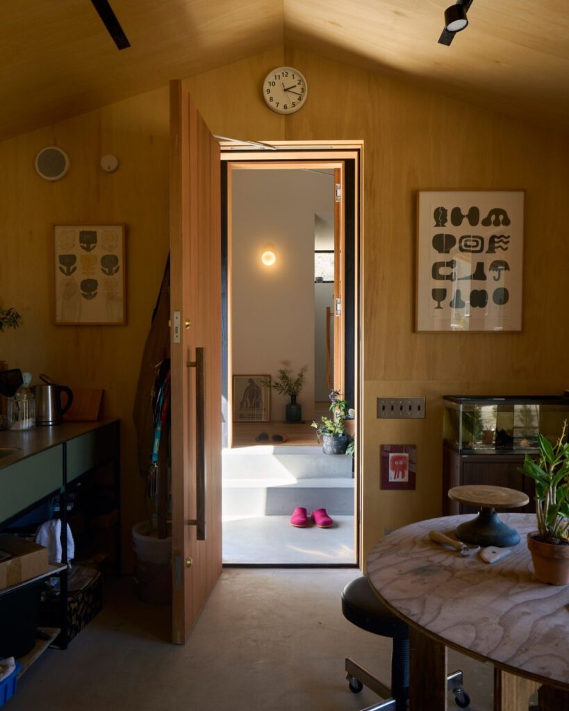 Interior of the single-story studio in Onomichi House, showcasing plywood walls and a connection to the main building via a central door.