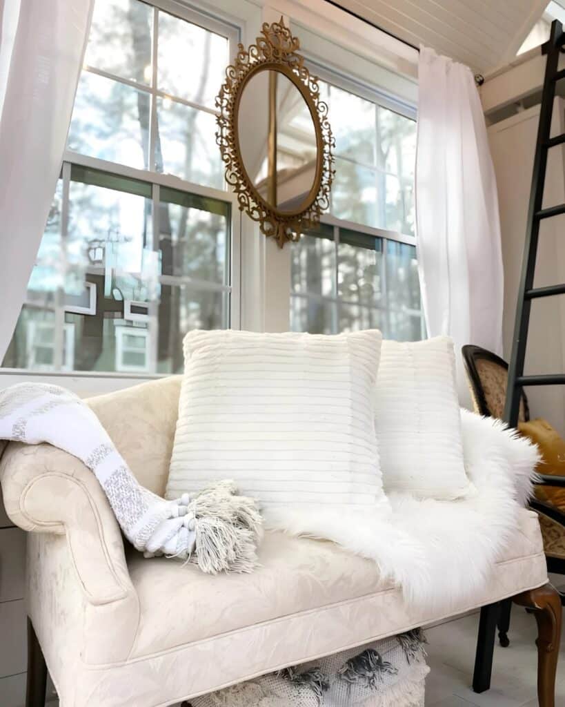 Close-up of a classic white tufted sofa in a tiny house with soft pillows and a gold ornate mirror on the wall.