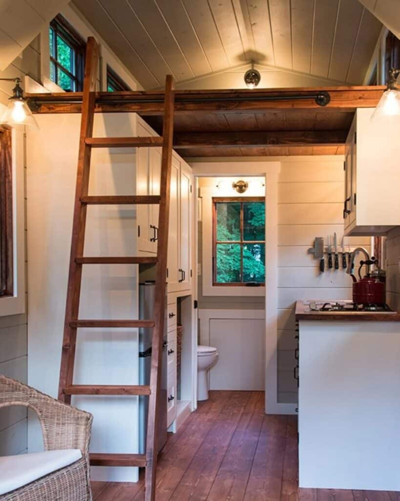 Full interior view from the living area toward the kitchen and bathroom, featuring the ladder, loft, and warm lighting.