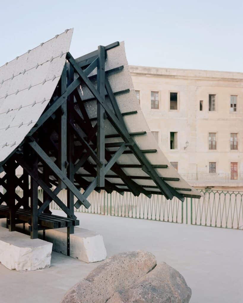 Side profile of the charred wood truss system supporting the lava stone roof, with a historic building in the background.