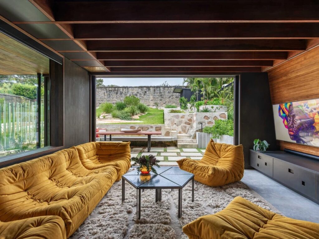 Living room with a plush shag rug, yellow modular sofas, and a wide opening to a stone-paved courtyard and garden.