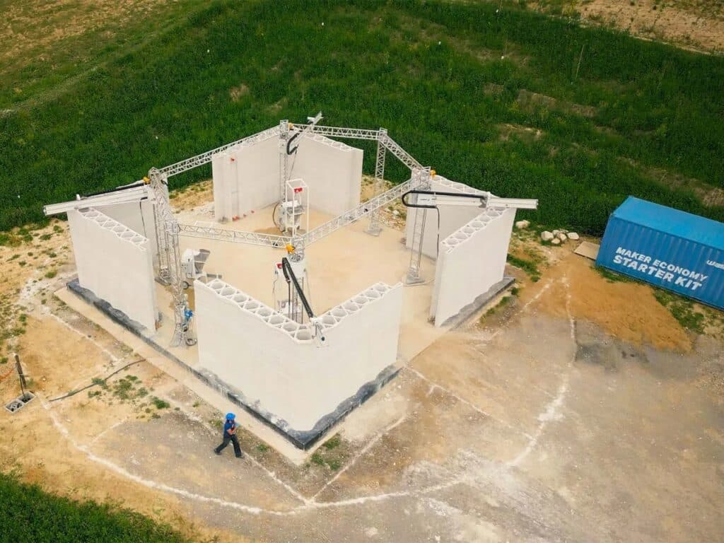 Aerial perspective of the 3D printing site with a "Maker Economy Starter Kit" shipping container nearby in a rural field.