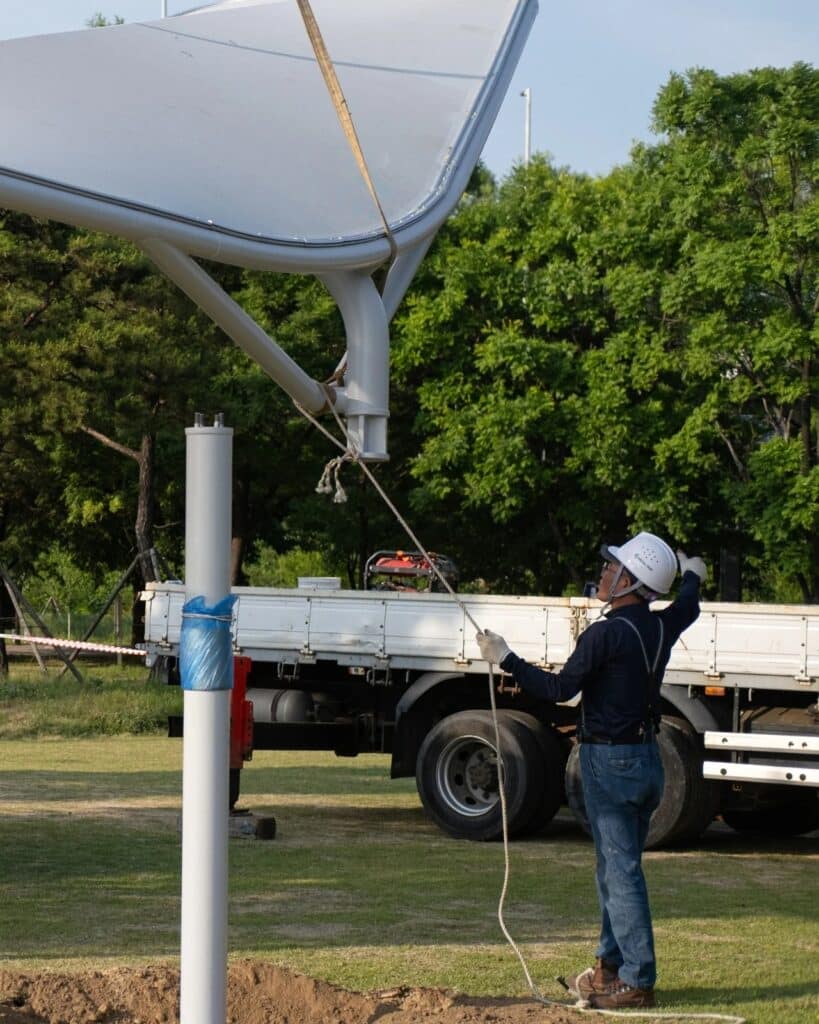 Construction workers installing a Seoul Wing canopy using ropes and light machinery in a park.