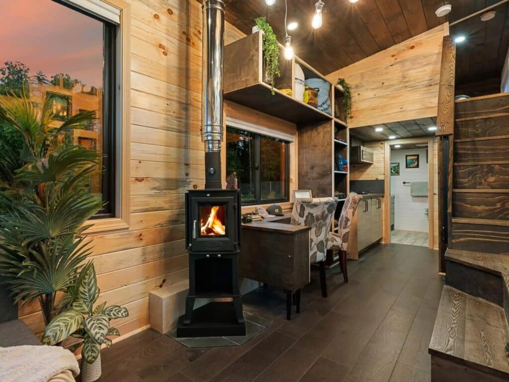 Open-plan interior of The Park tiny home featuring a wood-burning stove, workspace, and wooden stairs.