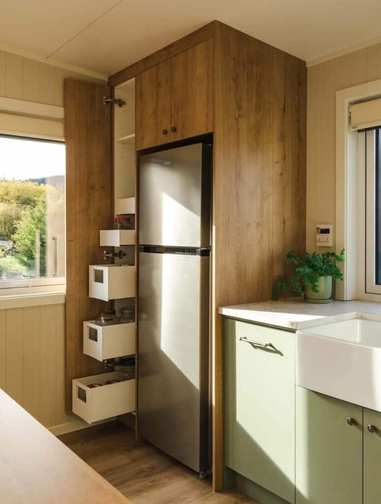 Pull-out pantry storage drawers next to a stainless steel refrigerator in a wooden cabinet unit.