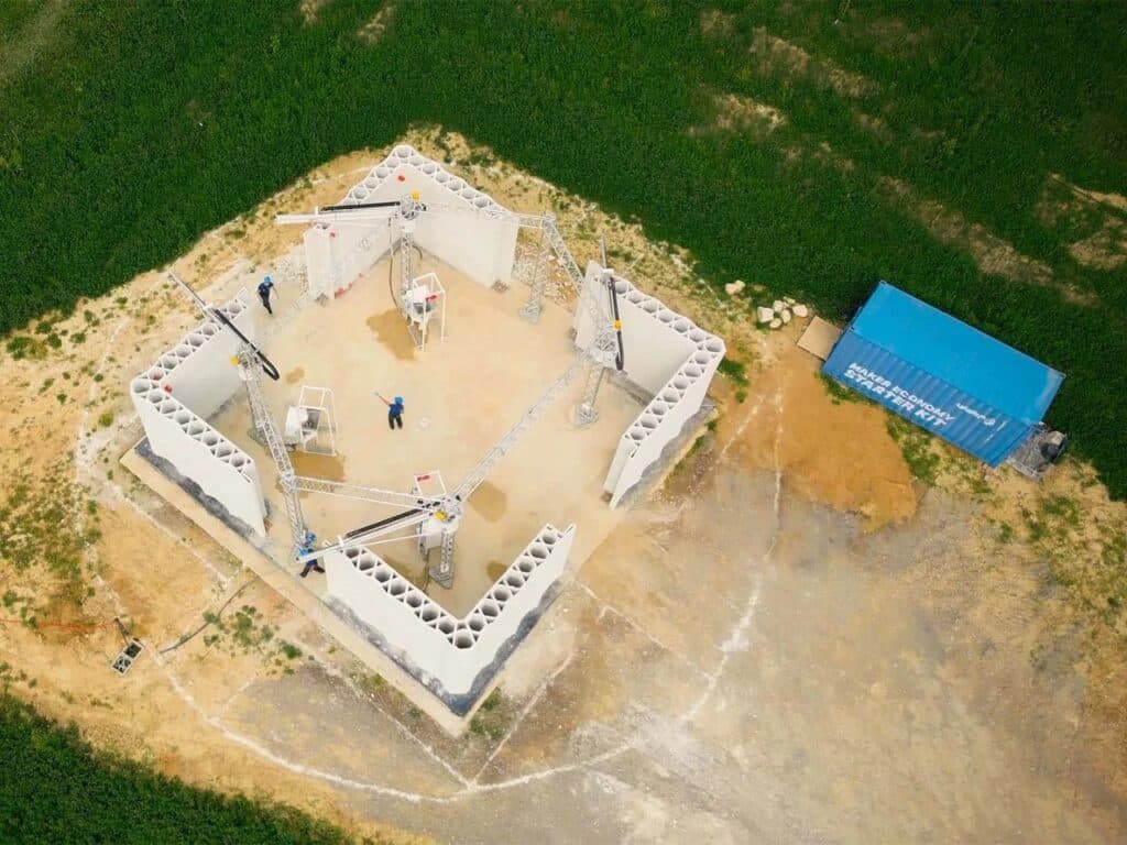 Top-down view of the 3D-printed farm site showing workers coordinating the printing of four interconnected wall sections.