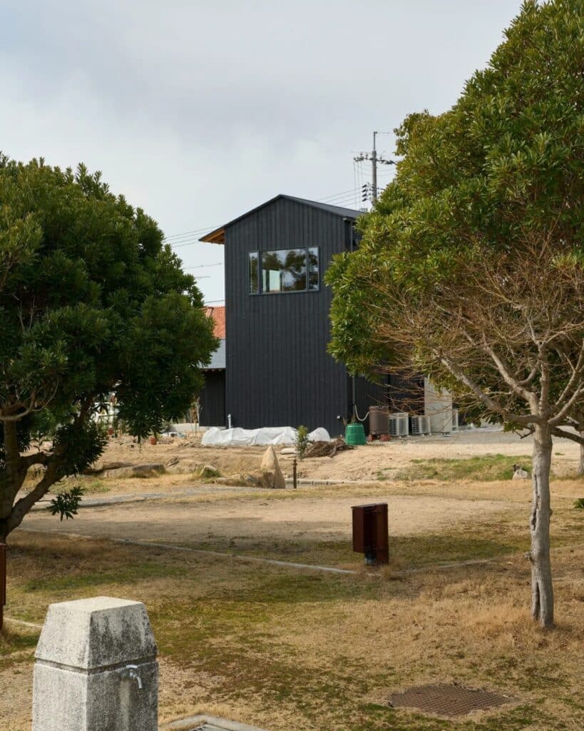 Side view of the tall main house structure of Onomichi House featuring a single large upper-floor window overlooking the site.
