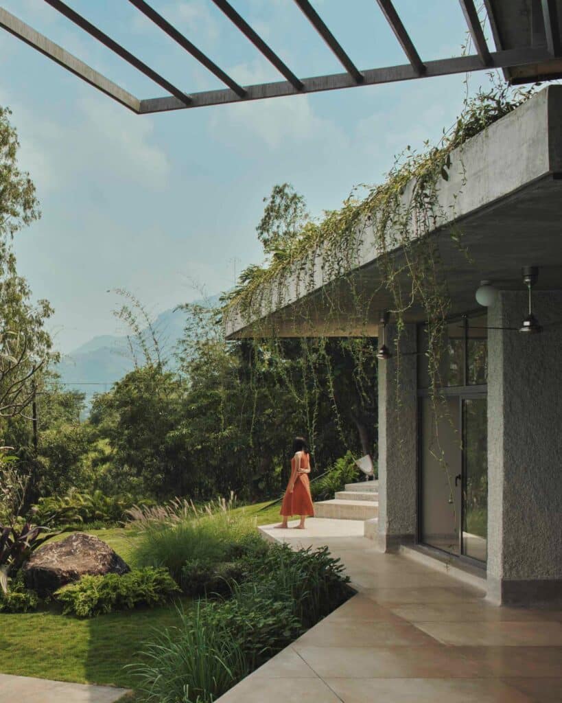 A person standing on a concrete terrace of a hilltop house looking out at distant mountains.