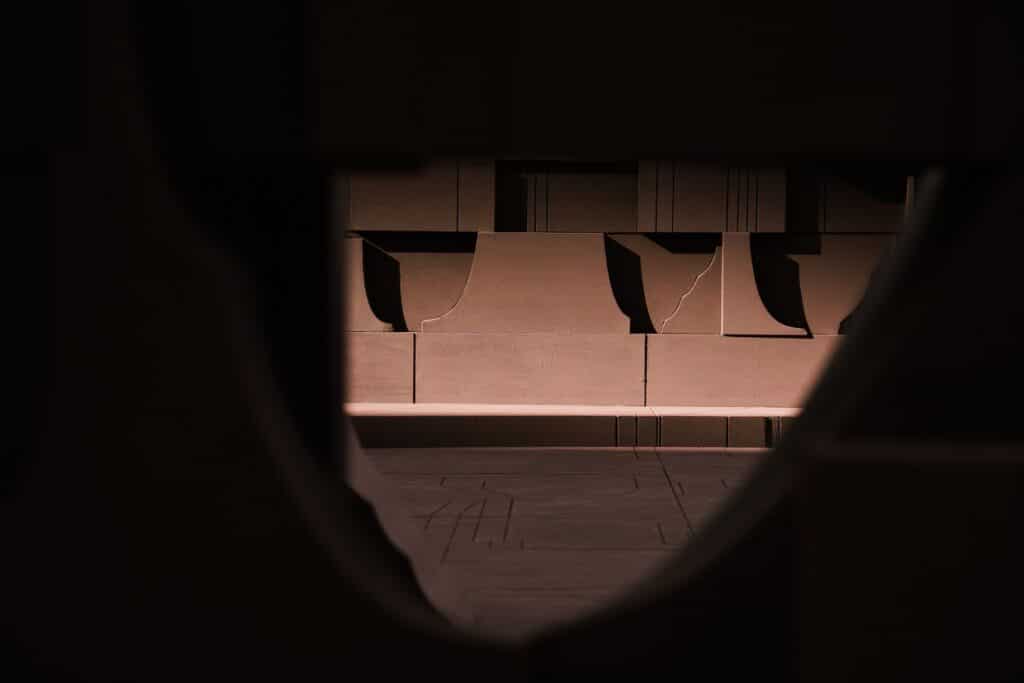 A dark, moody silhouette view looking through a geometric opening within the "In the Assembly of Loved Ones" installation.