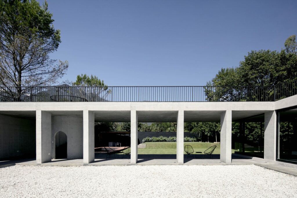A long shot of the concrete pillar structure separating the white gravel courtyard from the green grass garden.