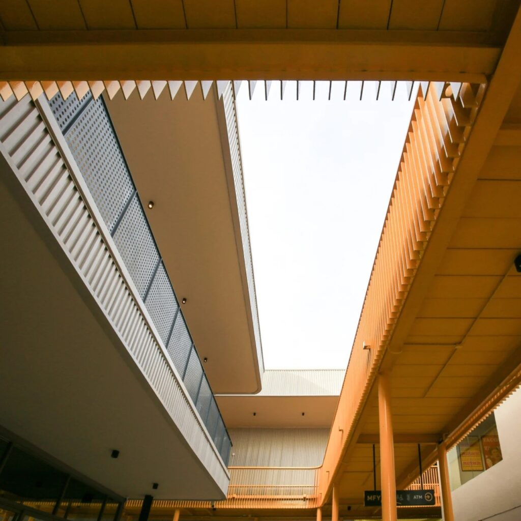 Low-angle architectural view of a multi-level urban retail space featuring modern orange louvers and minimalist white structures under an open sky.