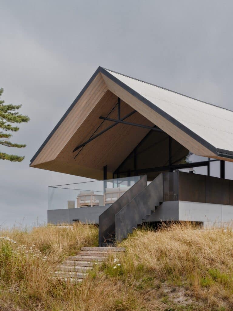 Detailed view of the gabled roof structure and outdoor terrace with glass railings overlooking the grassy dunes.