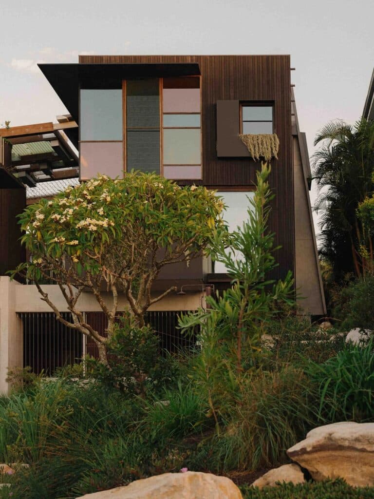 Exterior facade of Holocene House with dark charred timber cladding and native Australian coastal vegetation in the foreground.