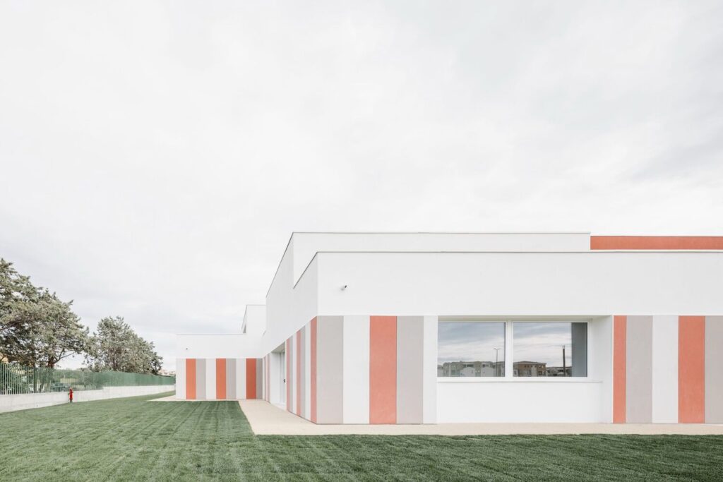 Perspective view of the nursery's white facade showing the rhythmic colored panels and lawn.