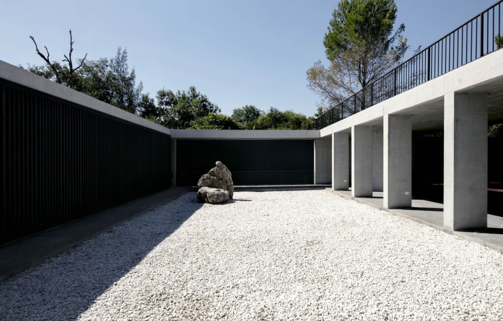 An internal courtyard featuring white gravel, a large natural rock, and a black boundary wall under a concrete overhang.