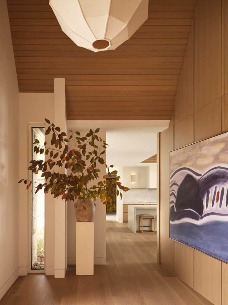 Interior hallway featuring light wood flooring, a sculptural plant arrangement, and contemporary abstract art on wood-paneled walls.