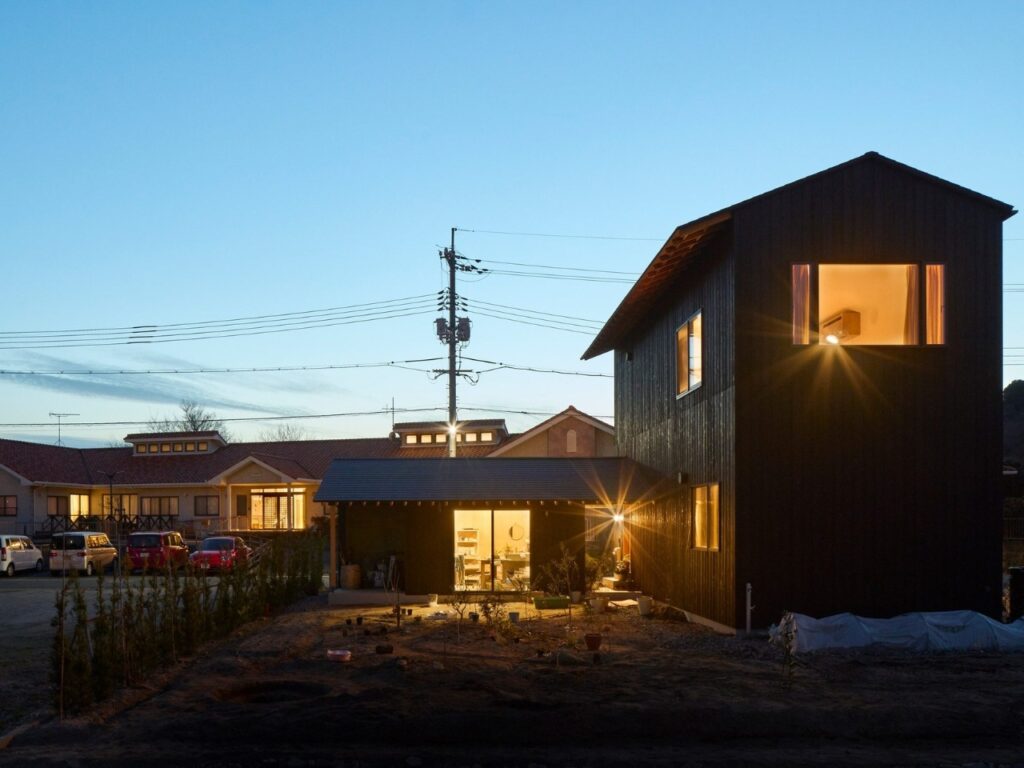 Exterior twilight shot of Onomichi House with warm internal lights glowing through the windows against a dark blue sky.