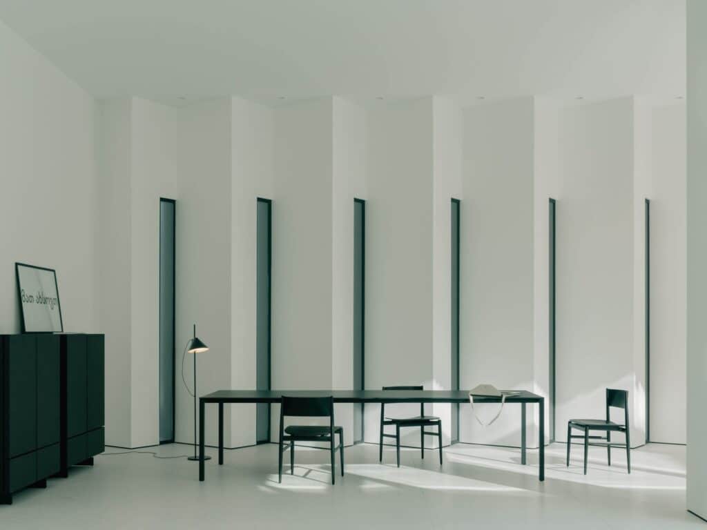 High-ceiling minimalist living area with abstract white walls and long black dining table.