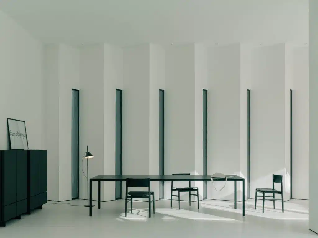 High-ceiling minimalist living area with abstract white walls and long black dining table.