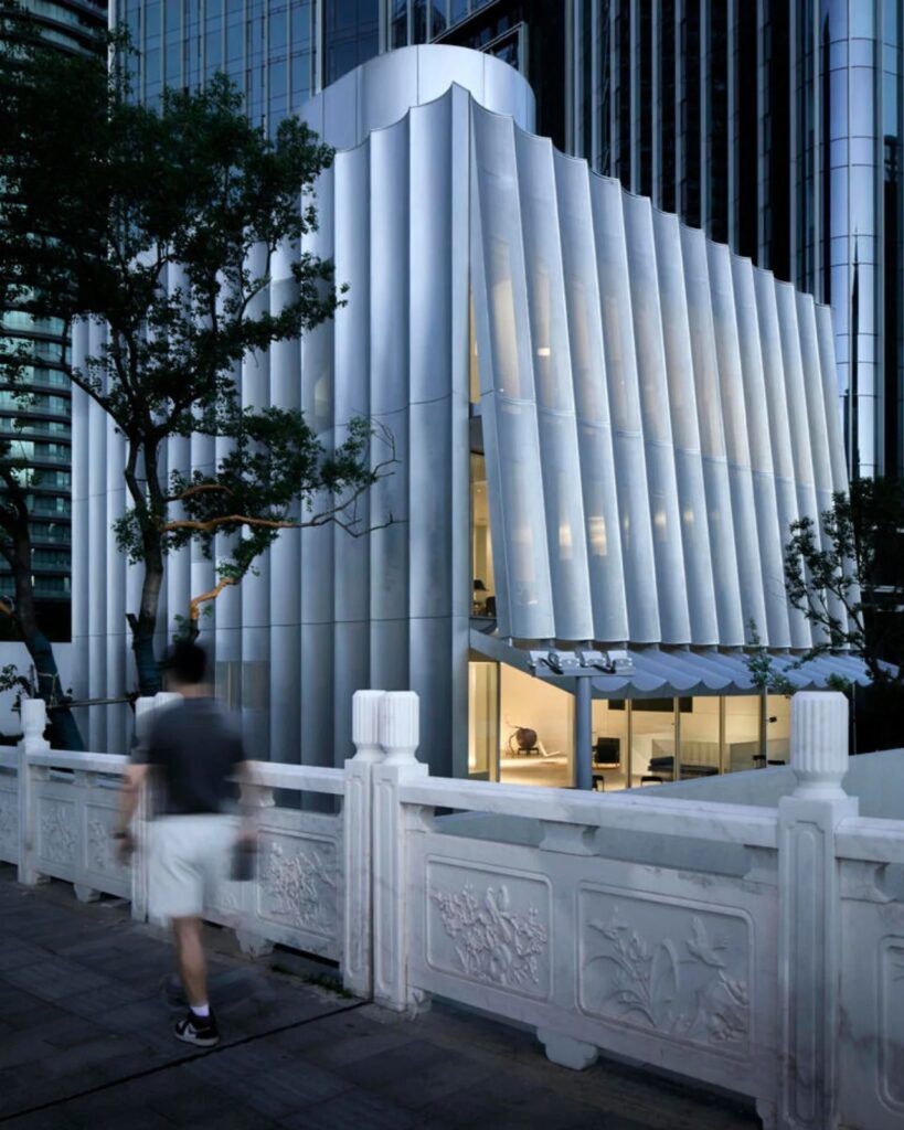 Dusk view of the Hangzhou Empathy Museum with glowing interior lights visible through the wavy metal cladding.
