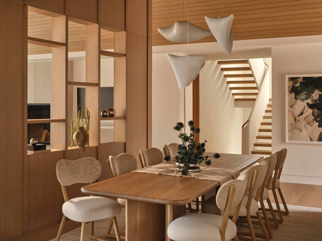 Contemporary dining area with a wooden table, sculptural pendant lights, and a view of the minimalist white staircase.