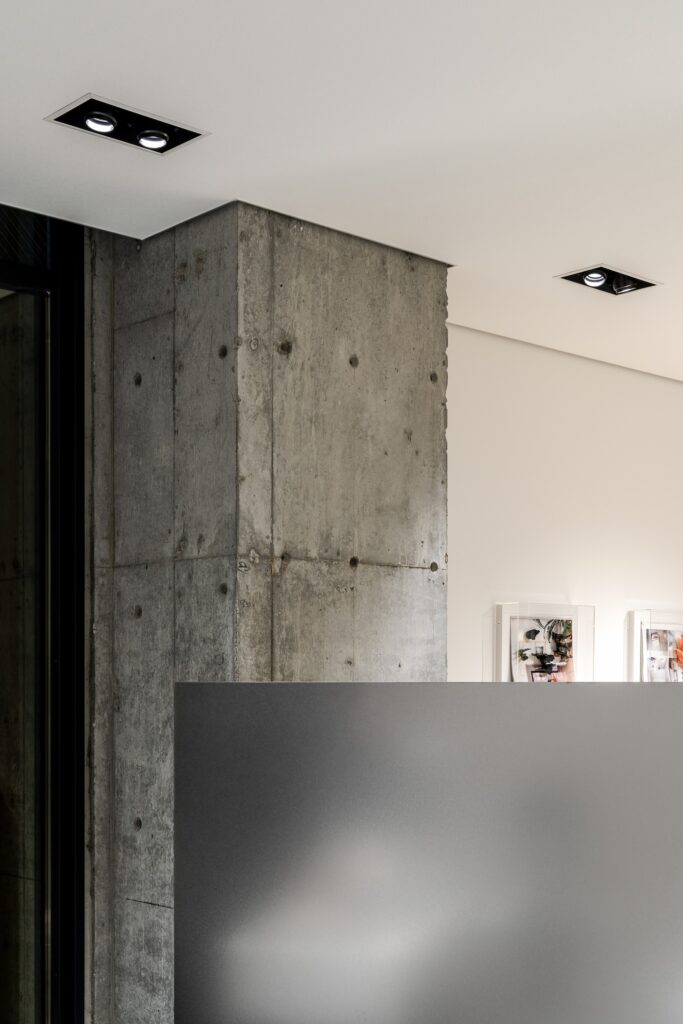 Close-up of a raw concrete pillar contrasting with a smooth white ceiling and modern recessed lighting.