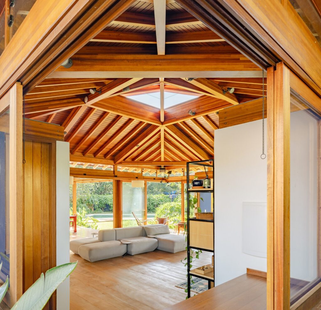 Interior view of a high-ceilinged wooden pavilion with exposed beams and a central skylight.