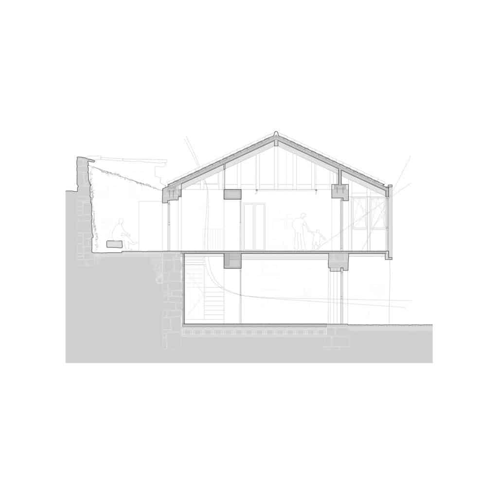 Architectural cross-section of the rehabilitated house showing the two levels and the relationship with the sloped terrain.