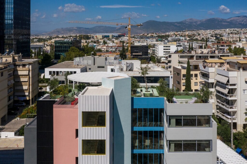 Wide aerial view of the Art1 office building within its city context, showing the colorful rooftop gardens and the surrounding urban landscape.