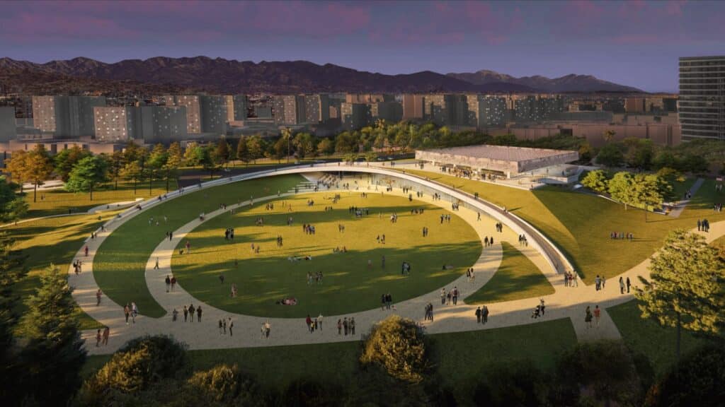 An aerial architectural rendering of a modern circular park pavilion at La Brea Tar Pits, featuring a large grassy oval surrounded by walking paths and people, with the Los Angeles skyline and mountains in the background at sunset.