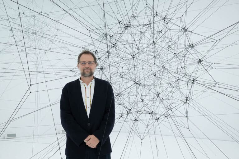 Tomás Saraceno standing in front of a large geometric string installation