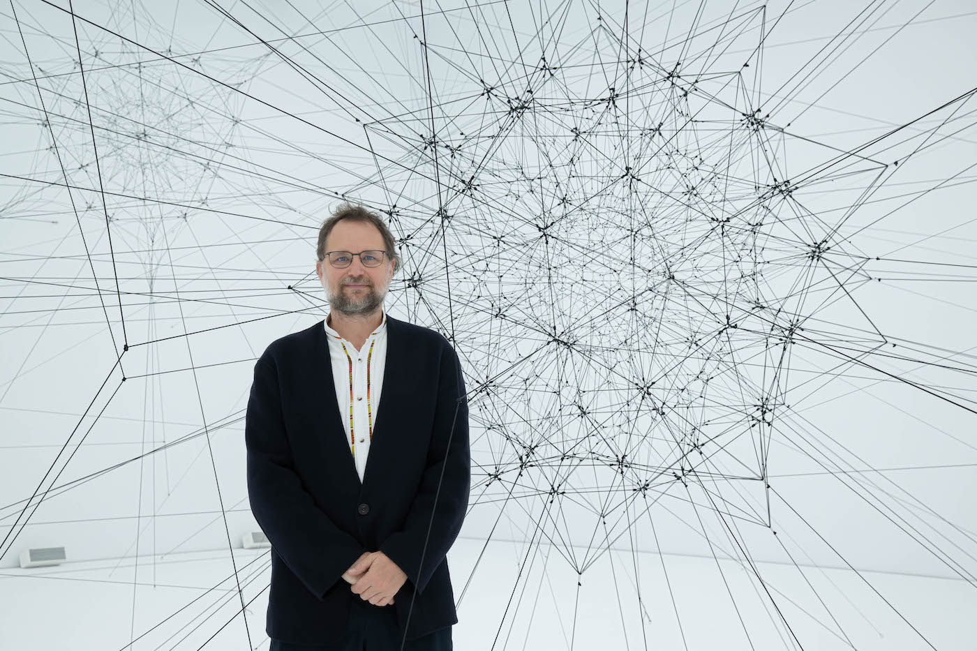 Tomás Saraceno standing in front of a large geometric string installation