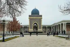 Front view of Imam al-Bukhari Complex mausoleum with blue dome and visitors in courtyard near Samarkand