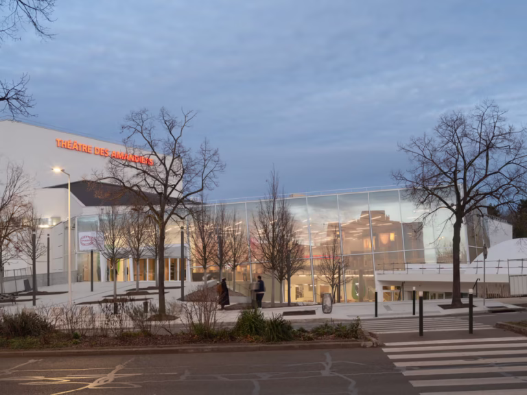 Theatre rehabilitation project exterior showing illuminated entrance and transparent glass facade at dusk.