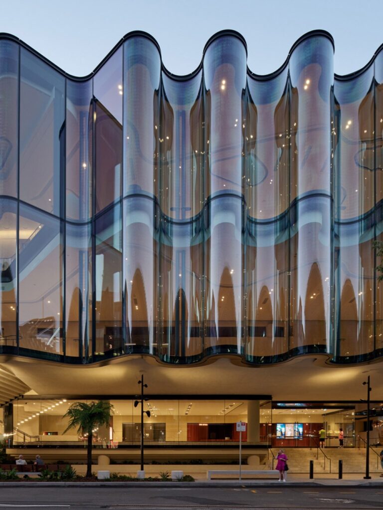Close up of the wavy glass facade of the Glasshouse Theatre reflecting the surroundings.
