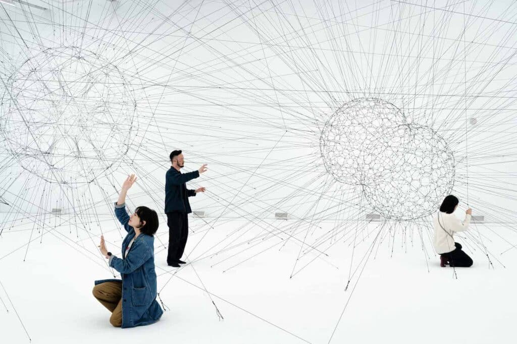 Visitors engaging with an interactive architecture installation made of tensile black strings